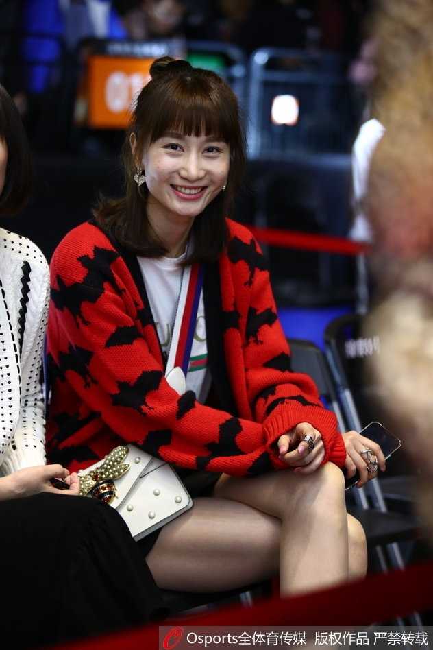 这位观战的女士身穿宽松的黑色卫衣，搭配时尚的棒球帽，正用手机自拍记录下这个难忘的全明星之夜，背景是模糊的球场灯光和人海。