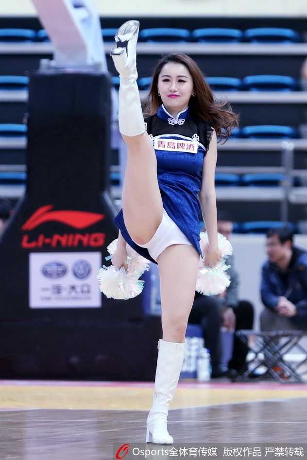 一位戴着白色毛球发饰的篮球宝贝双手叉腰侧身站立，紧身表演服勾勒出纤细的腰肢，她凝视镜头的眼神既甜美又充满自信，极具感染力