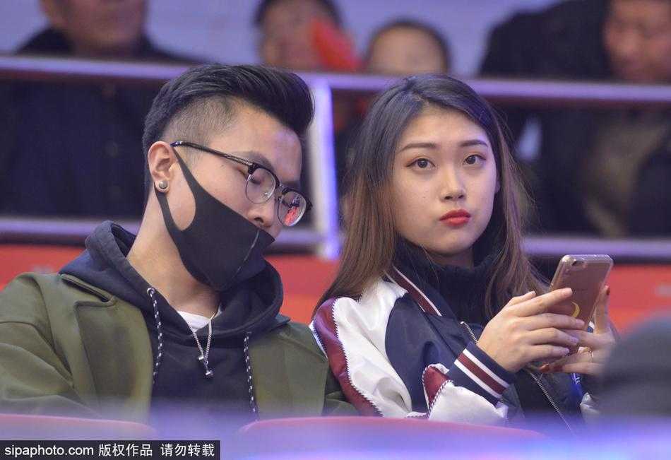 赛场灯光下，一位面容姣好的女球迷静静坐在看台上，她乌黑的长发披肩，眼神清澈而专注，仿佛世间万物都不及场上那个飞奔的身影重要，高挺的鼻梁和精致的侧脸在人群中显得格外醒目。