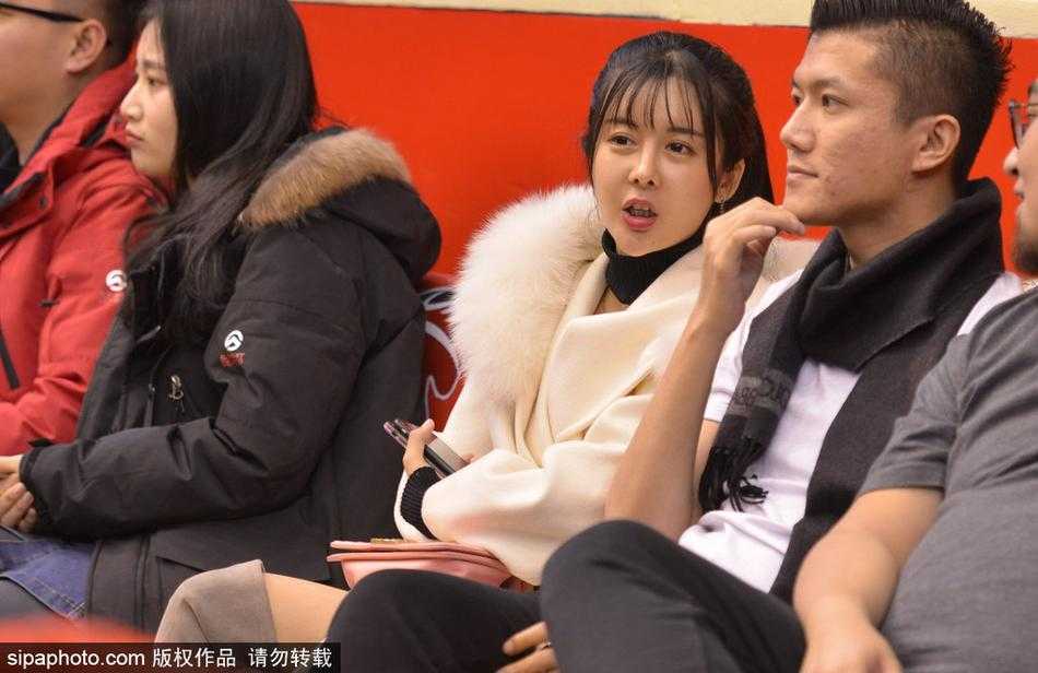 一位面容清秀的女球迷披散着长发，双手轻托脸颊，眼神专注地望向赛场中央，仿佛此刻世界只剩下她与那片熟悉的篮球场。